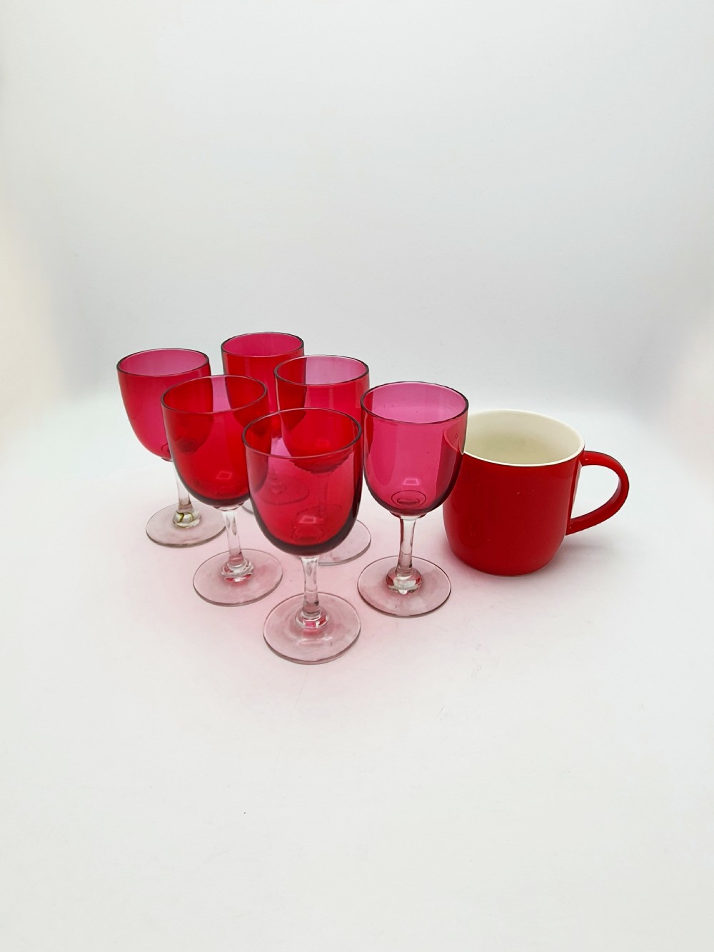 A set of six Victorian hand-blown wine glasses featuring deep cranberry red rounded bowls atop clear glass stems and circular bases. View VI