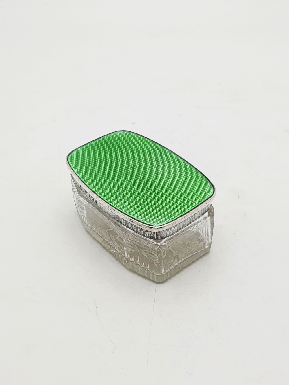 A rectangular clear etched glass dressing table jar topped with a sterling silver rim and a bright green guilloche enamel lid.