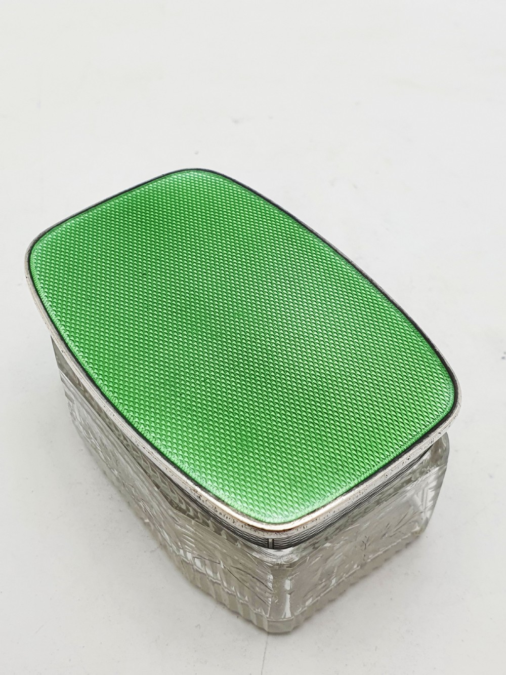 A rectangular clear etched glass dressing table jar topped with a sterling silver rim and a bright green guilloche enamel lid. View II