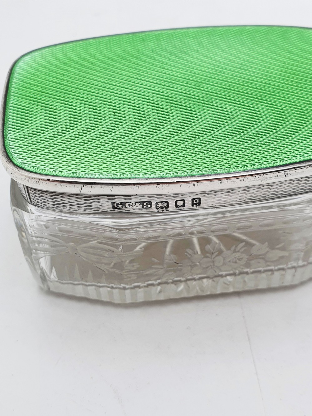 A rectangular clear etched glass dressing table jar topped with a sterling silver rim and a bright green guilloche enamel lid. View IV