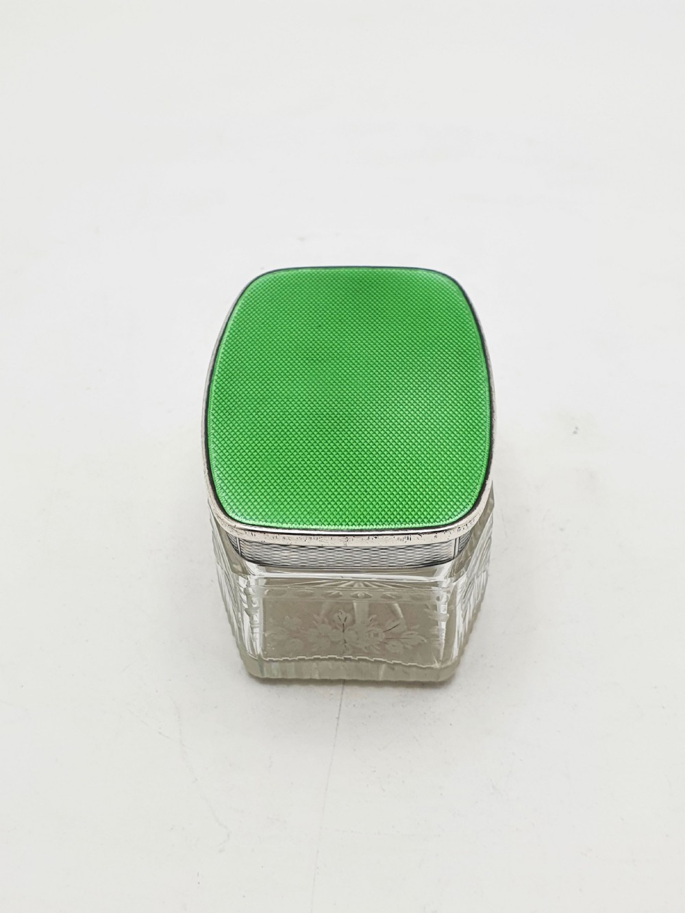A rectangular clear etched glass dressing table jar topped with a sterling silver rim and a bright green guilloche enamel lid. View V