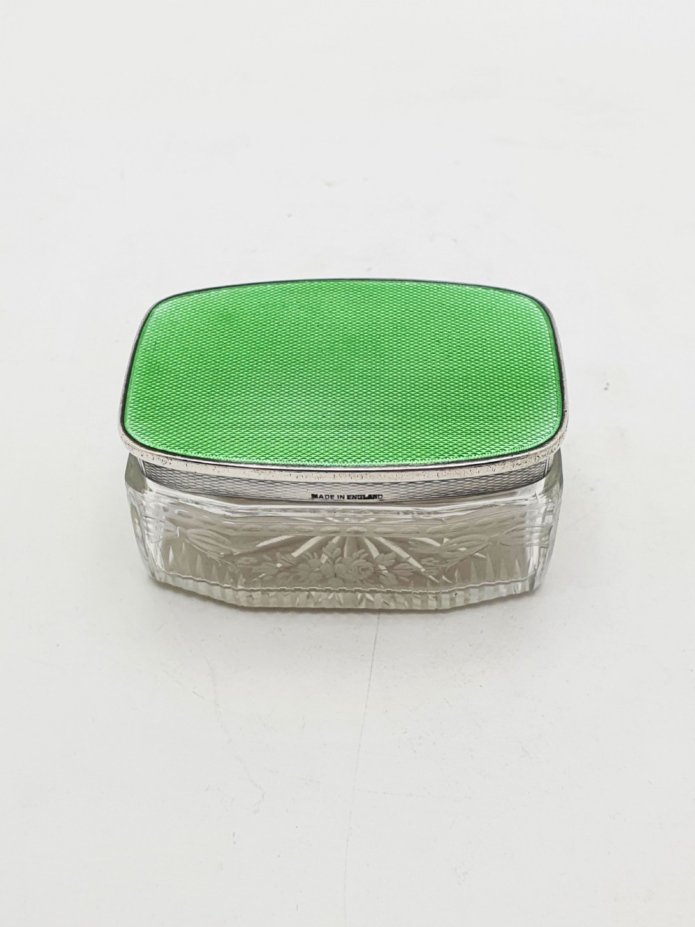A rectangular clear etched glass dressing table jar topped with a sterling silver rim and a bright green guilloche enamel lid. View VI