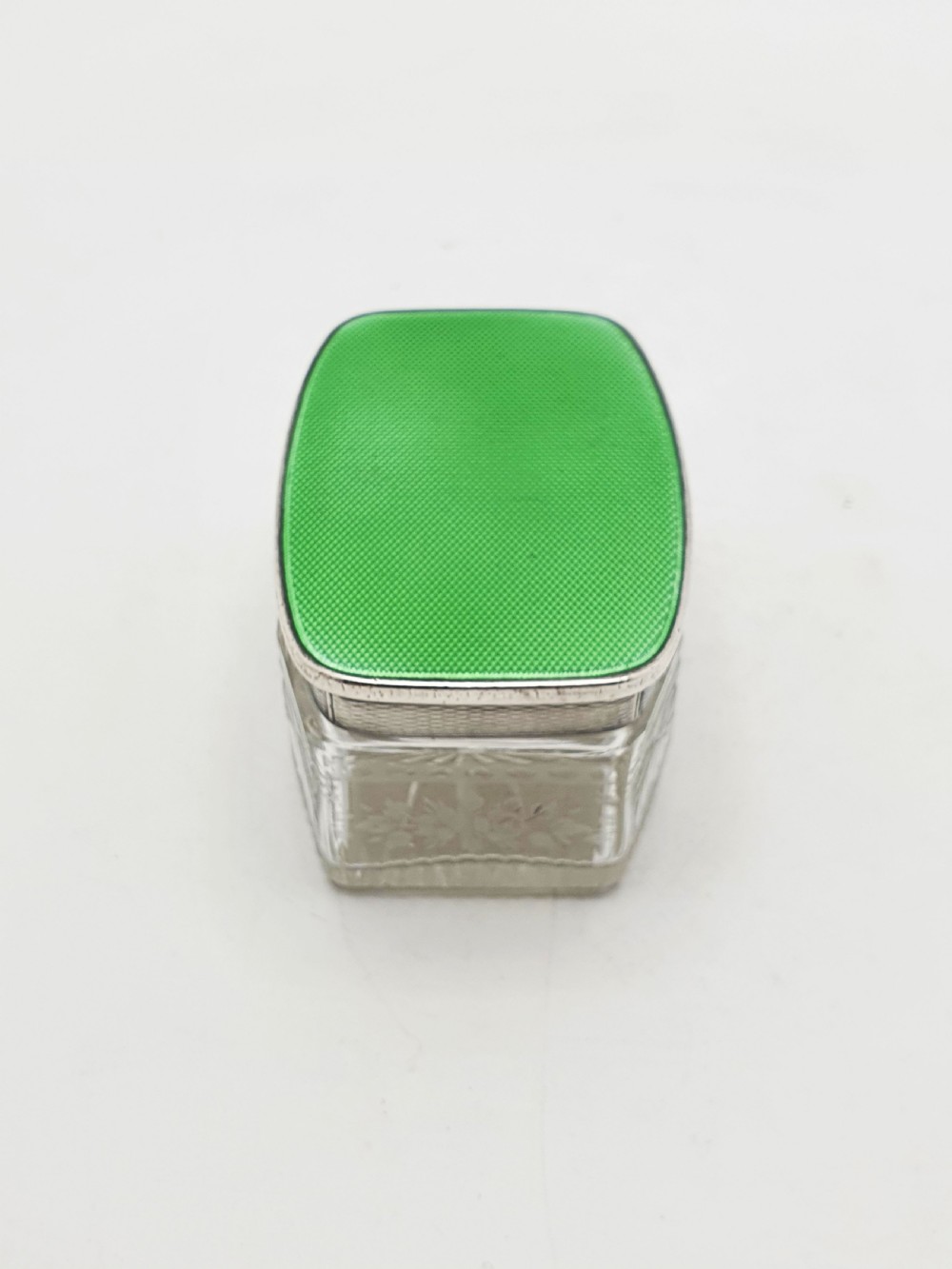 A rectangular clear etched glass dressing table jar topped with a sterling silver rim and a bright green guilloche enamel lid. View VII