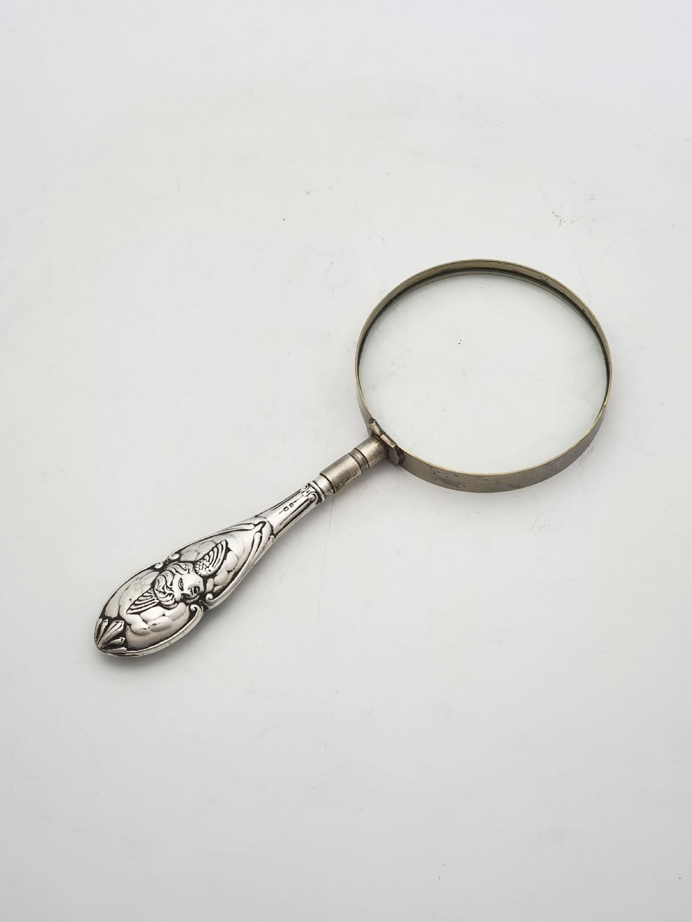 An Edwardian magnifying glass featuring a circular glass lens in a metal rim attached to an embossed sterling silver handle.