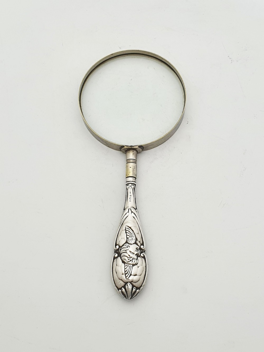 An Edwardian magnifying glass featuring a circular glass lens in a metal rim attached to an embossed sterling silver handle. View II