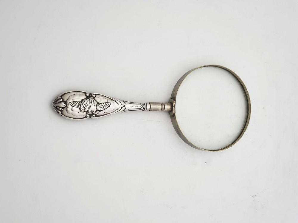 An Edwardian magnifying glass featuring a circular glass lens in a metal rim attached to an embossed sterling silver handle. View III