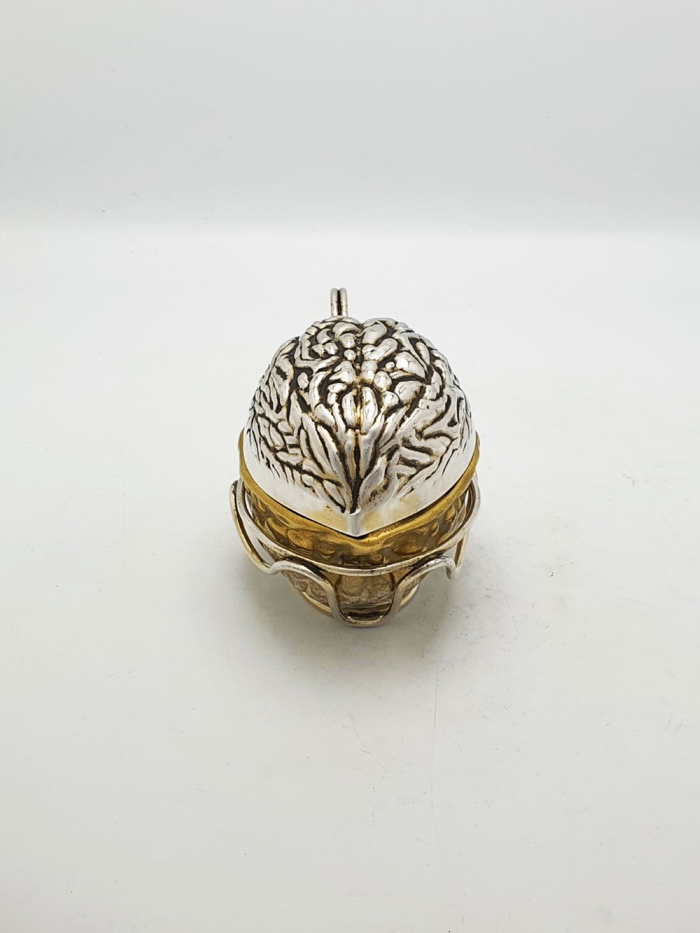 A late Victorian walnut-shaped metal condiment container featuring a textured silver lid and a brass lower shell resting within a wirework stand with a handle. View IV