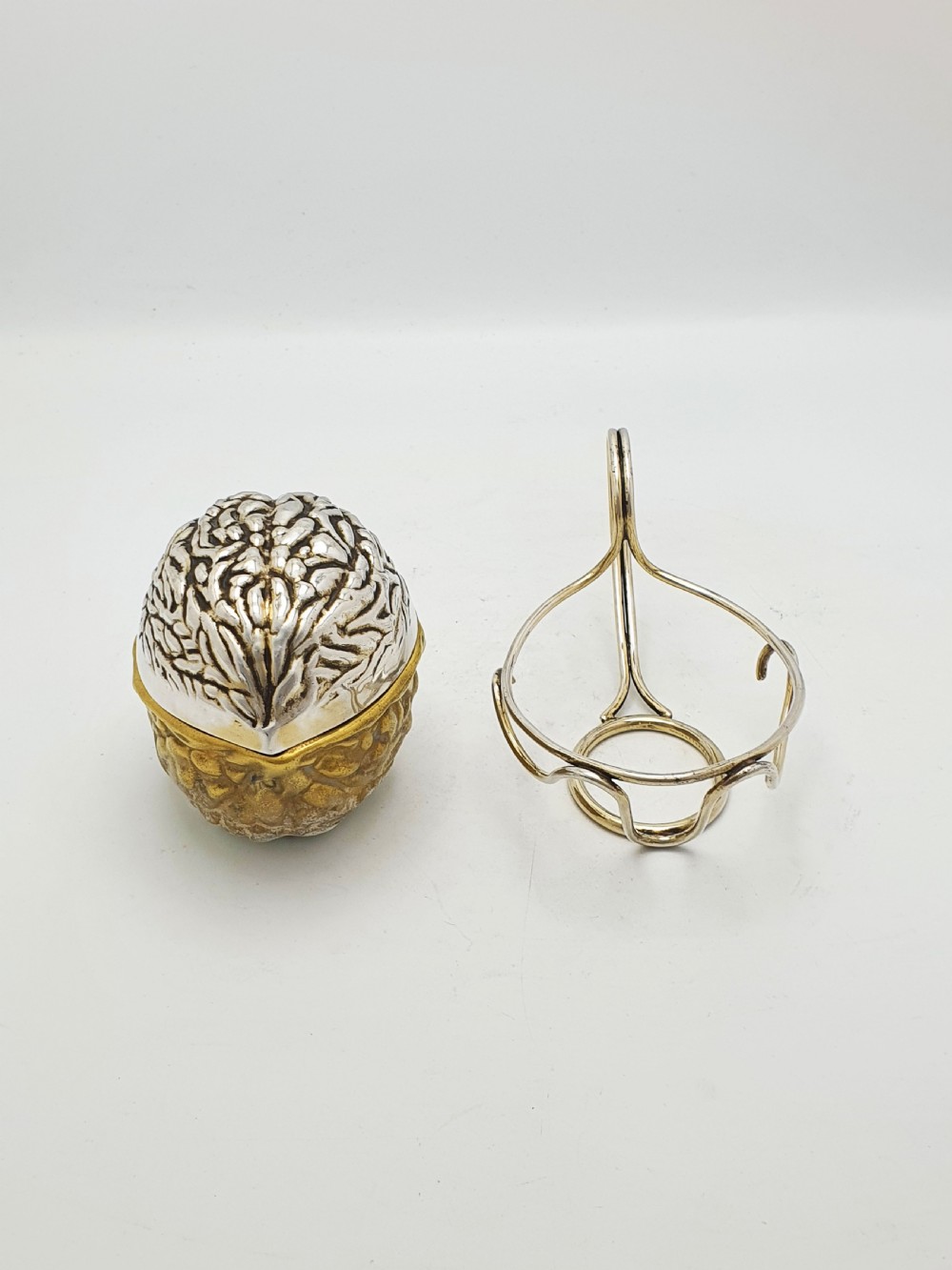 A late Victorian walnut-shaped metal condiment container featuring a textured silver lid and a brass lower shell resting within a wirework stand with a handle. View VIII