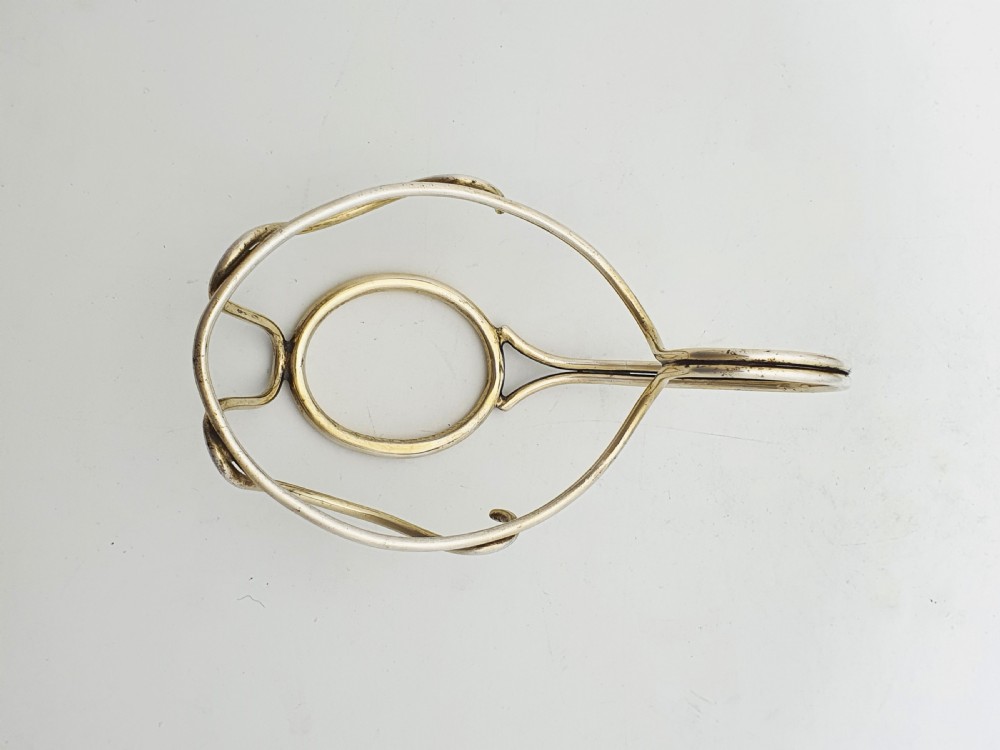 A late Victorian walnut-shaped metal condiment container featuring a textured silver lid and a brass lower shell resting within a wirework stand with a handle. View X
