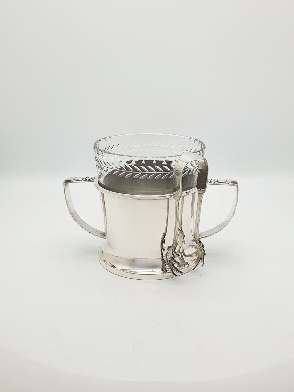 An Art Deco silver-plated ice bucket featuring twin handles, a removable cut-glass liner with a leaf pattern, and matching ice tongs. View III