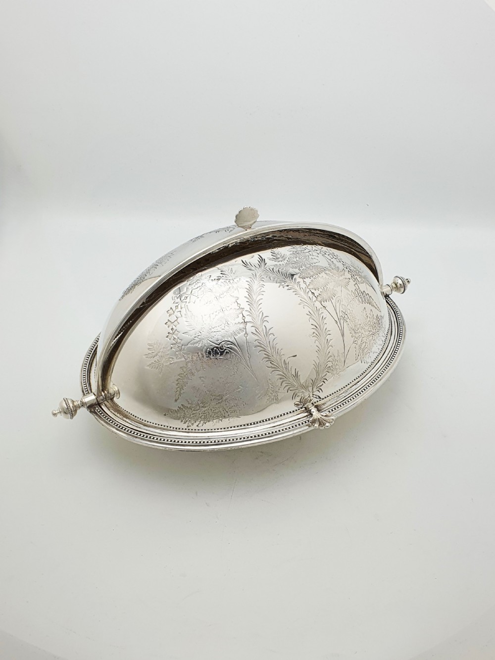 A late Victorian oval silver-plated rollover dish featuring bright-cut botanical engravings, a beaded rim, and side pivot handles.