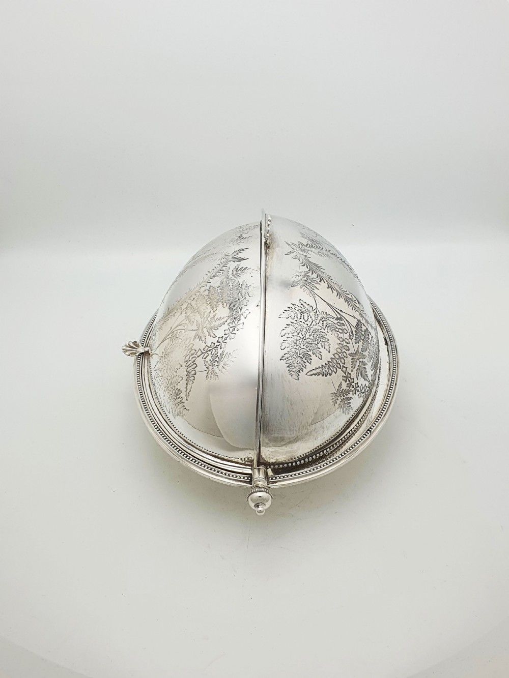 A late Victorian oval silver-plated rollover dish featuring bright-cut botanical engravings, a beaded rim, and side pivot handles. View V