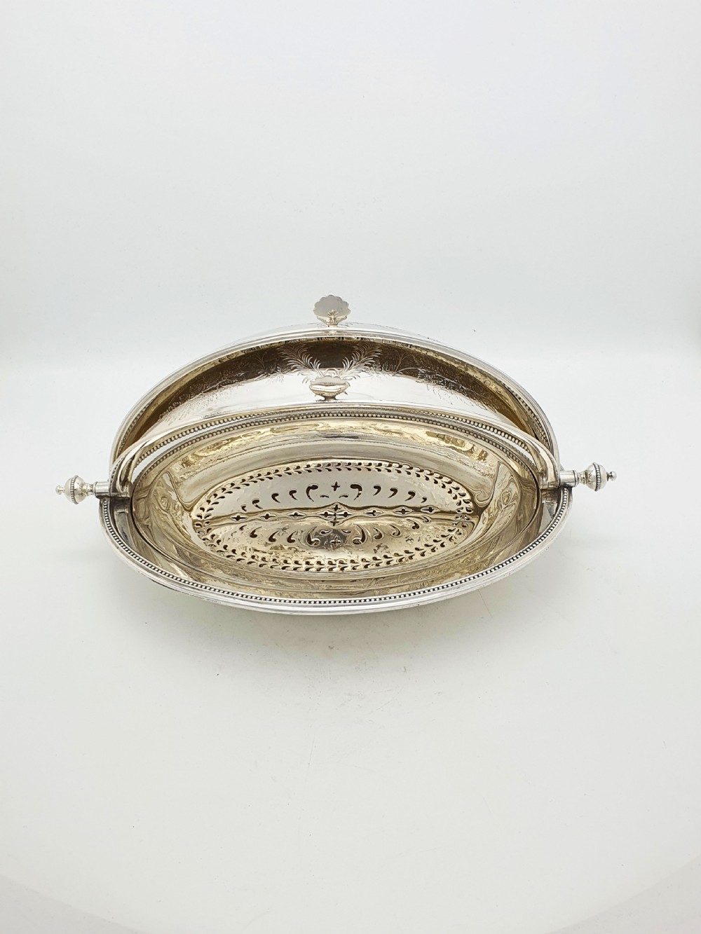 A late Victorian oval silver-plated rollover dish featuring bright-cut botanical engravings, a beaded rim, and side pivot handles. View VI
