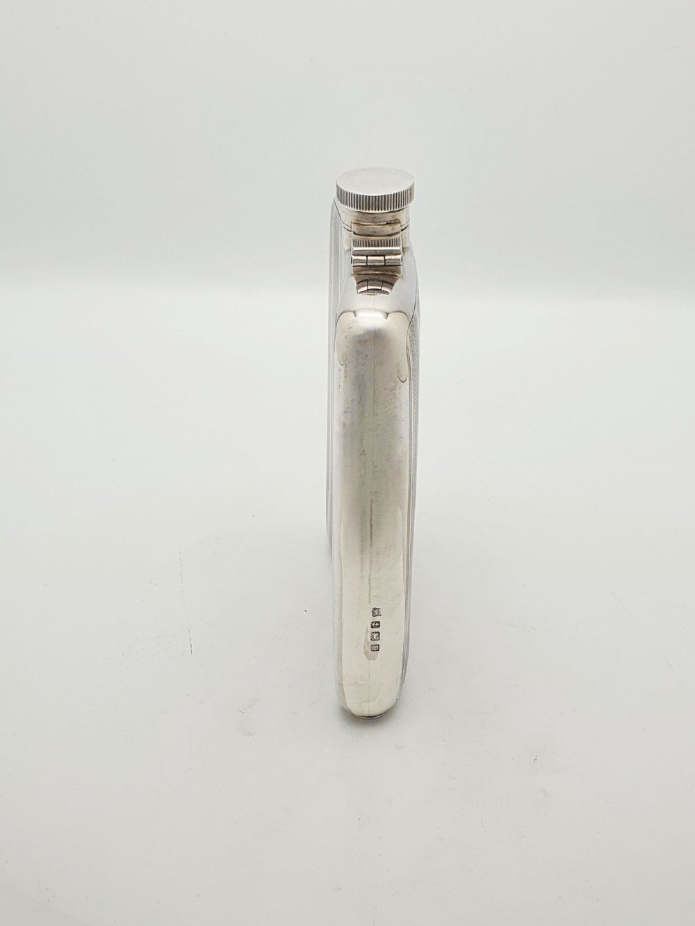 An Art Deco sterling silver hip flask featuring a curved rectangular body decorated with engine-turned linear engraving and a captive bayonet cap. View III