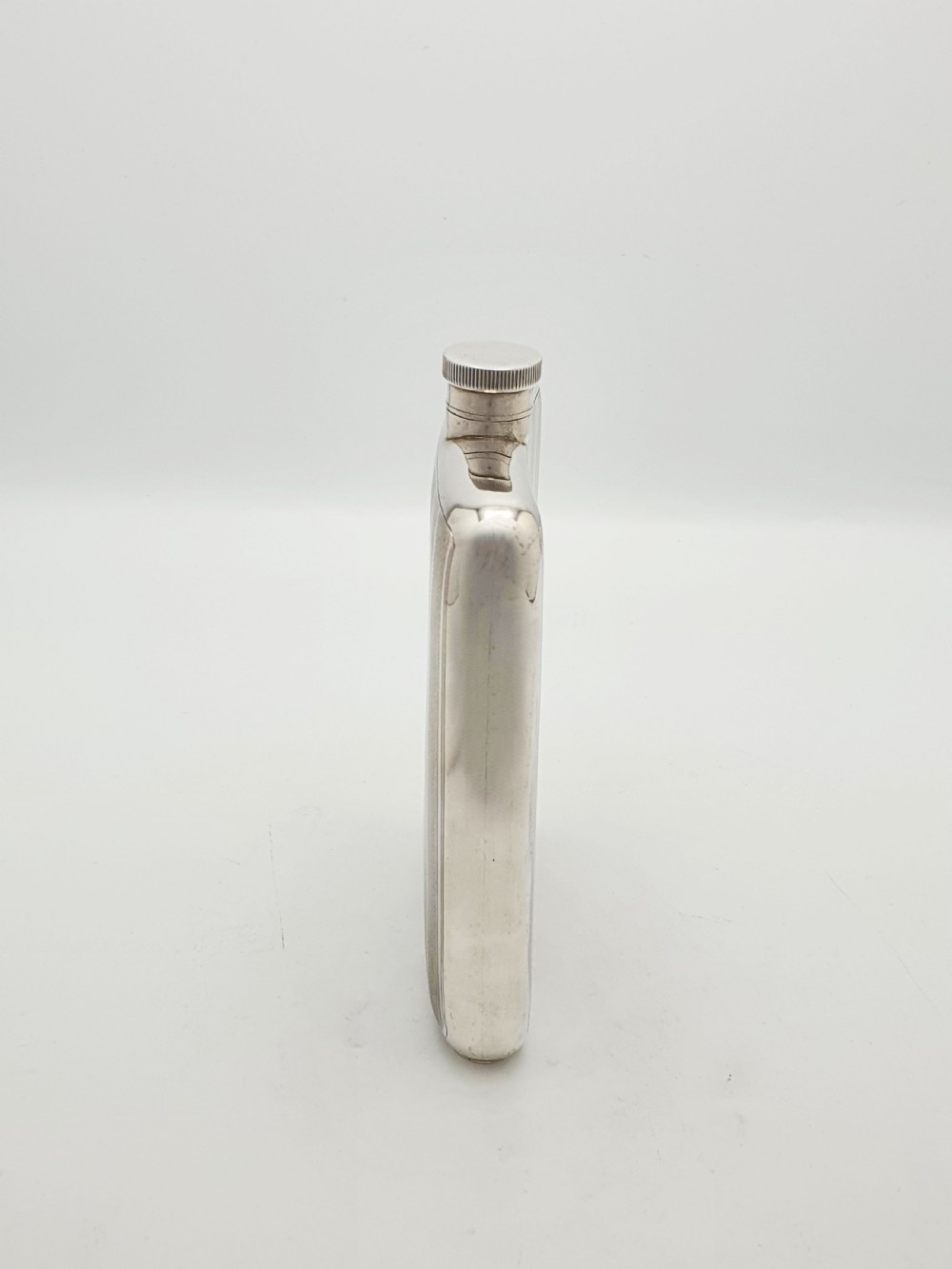 An Art Deco sterling silver hip flask featuring a curved rectangular body decorated with engine-turned linear engraving and a captive bayonet cap. View V