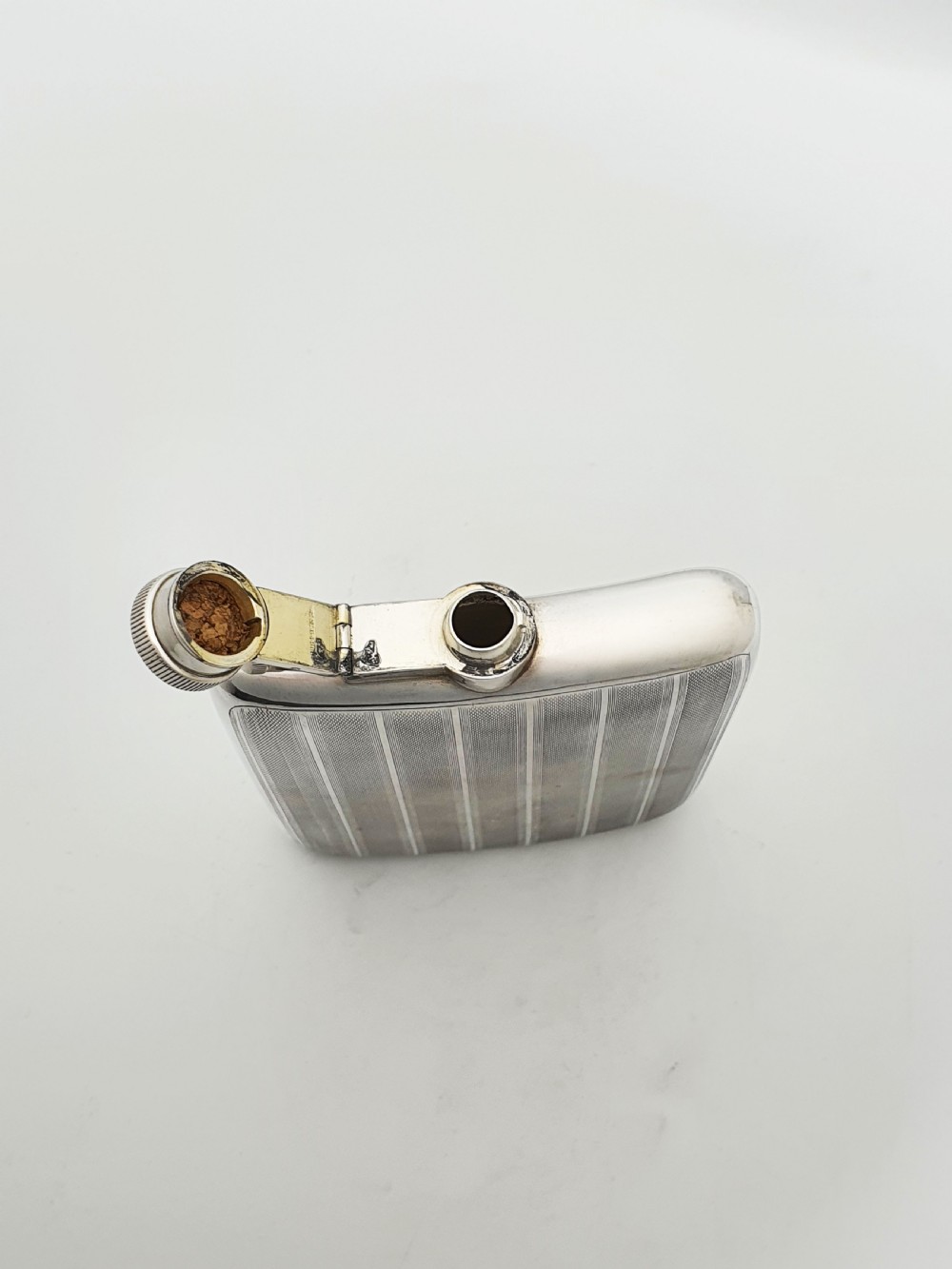 An Art Deco sterling silver hip flask featuring a curved rectangular body decorated with engine-turned linear engraving and a captive bayonet cap. View VII