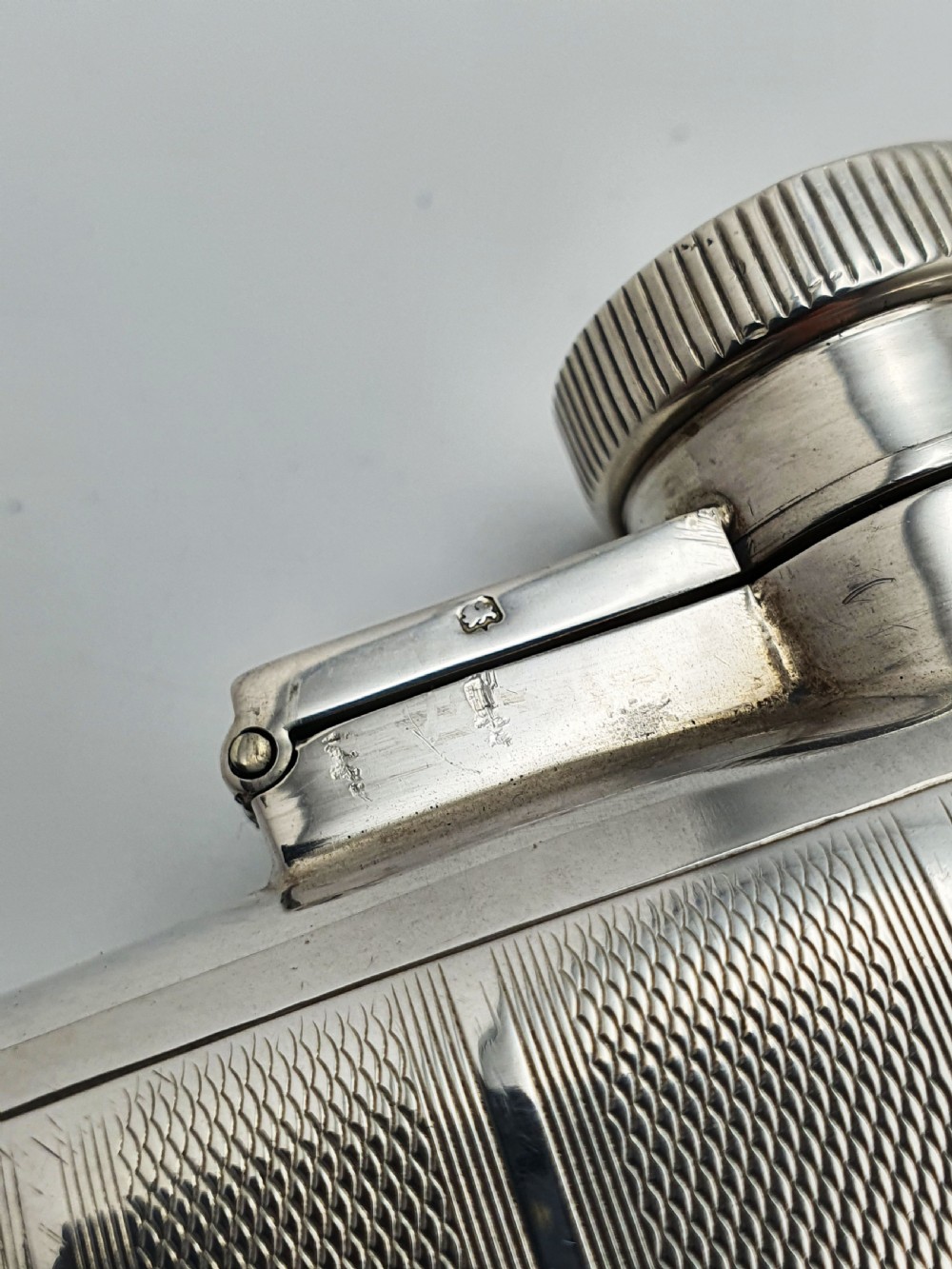 An Art Deco sterling silver hip flask featuring a curved rectangular body decorated with engine-turned linear engraving and a captive bayonet cap. View IX
