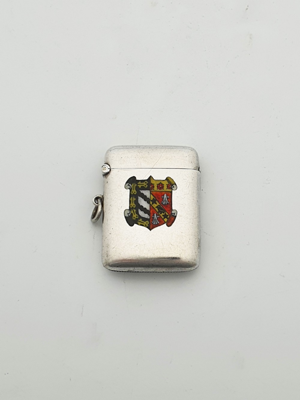 A rectangular sterling silver vesta case featuring a hinged top, side suspension ring, bottom striker, and a colourful heraldic enamel crest on the front. View II