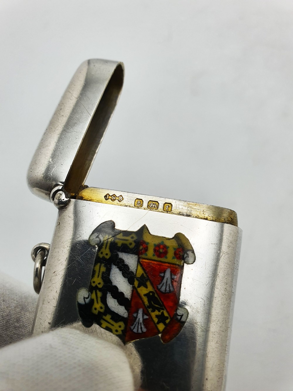 A rectangular sterling silver vesta case featuring a hinged top, side suspension ring, bottom striker, and a colourful heraldic enamel crest on the front. View IV