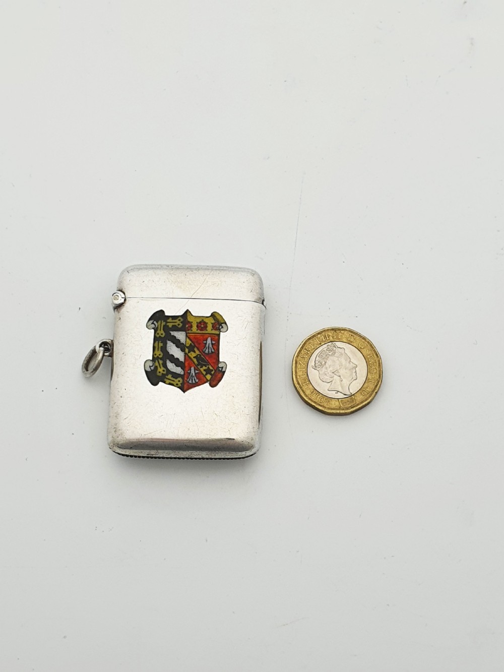 A rectangular sterling silver vesta case featuring a hinged top, side suspension ring, bottom striker, and a colourful heraldic enamel crest on the front. View VIII