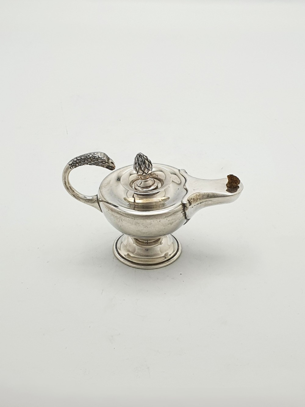 A sterling silver table lighter crafted in the shape of a classical Roman oil lamp with a serpent-shaped handle and pedestal foot. View II