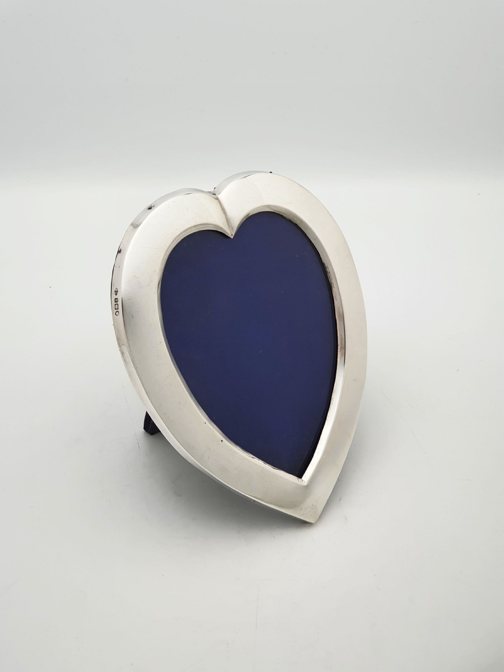 A heart-shaped Edwardian sterling silver picture frame with a smooth polished finish and dark blue display interior.