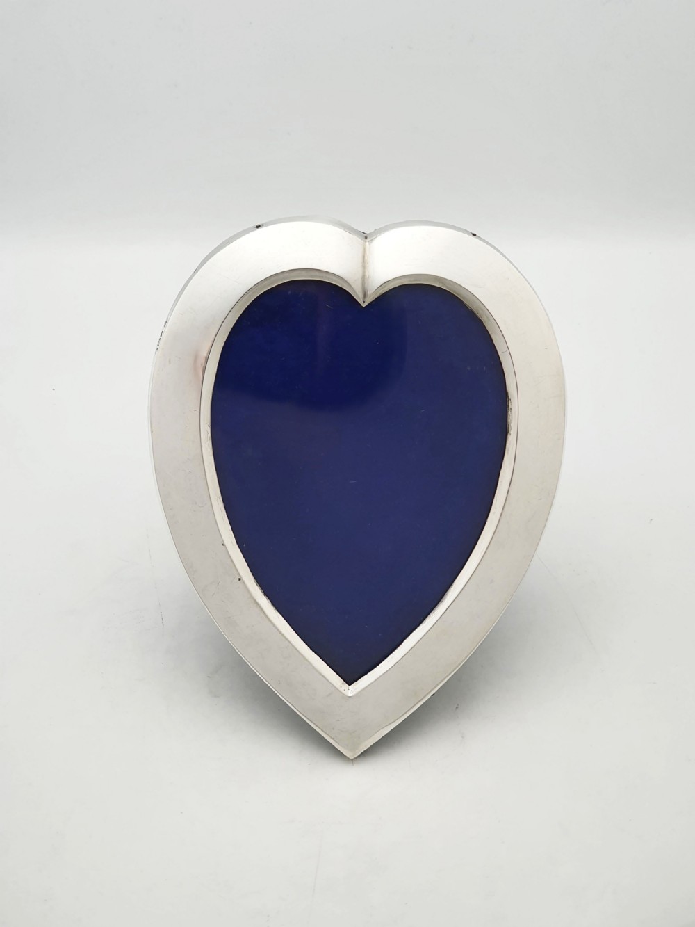 A heart-shaped Edwardian sterling silver picture frame with a smooth polished finish and dark blue display interior. View II