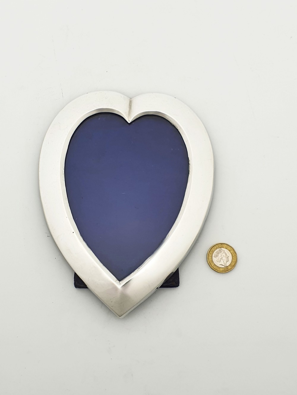 A heart-shaped Edwardian sterling silver picture frame with a smooth polished finish and dark blue display interior. View VII