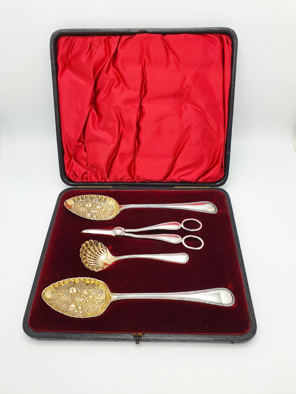 A Victorian silver-plated fruit serving set with embossed gilt bowls and grape shears, displayed inside a red velvet-lined presentation box.