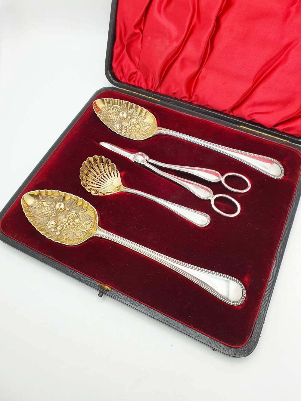 A Victorian silver-plated fruit serving set with embossed gilt bowls and grape shears, displayed inside a red velvet-lined presentation box. View II