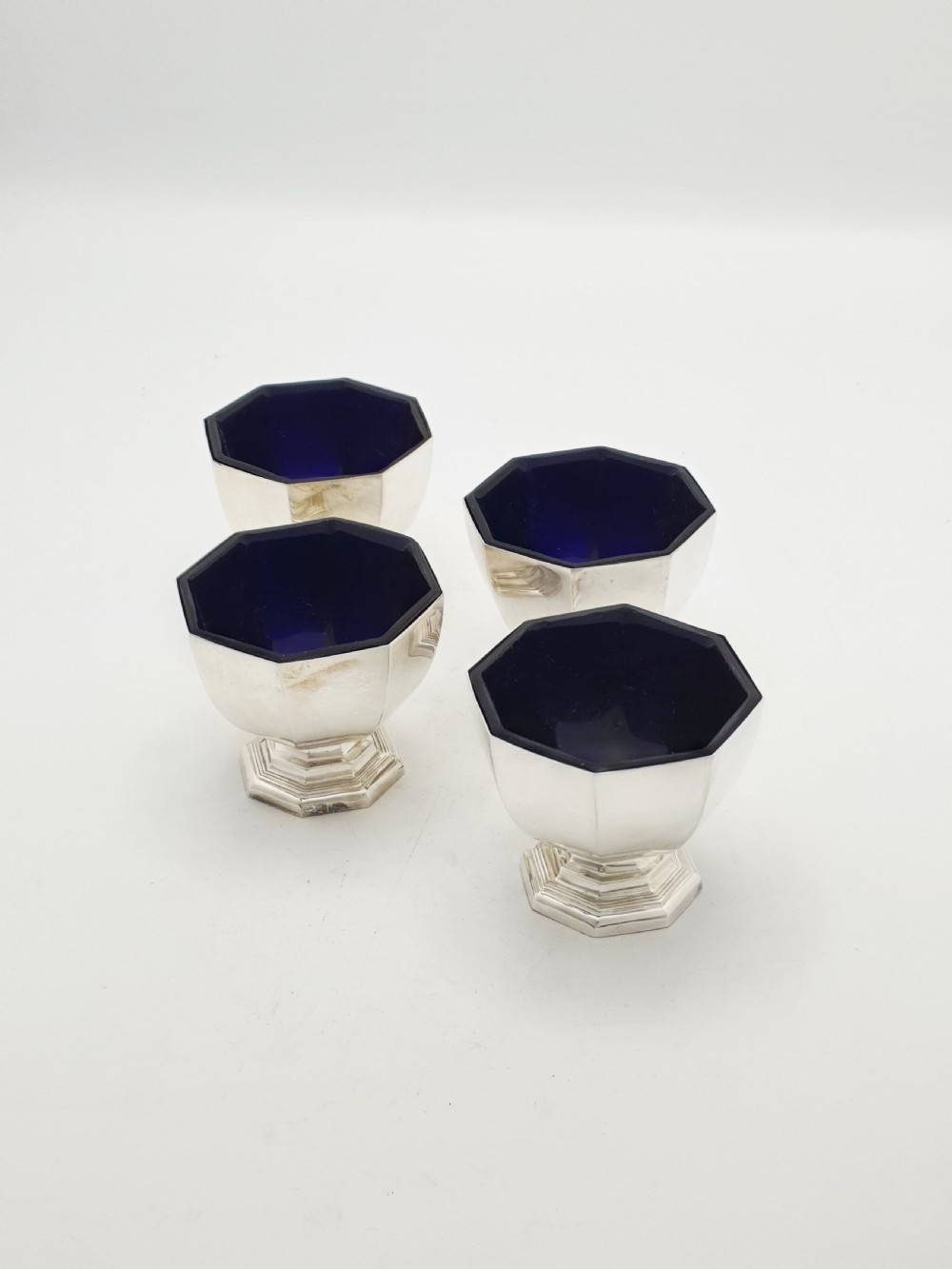 A set of four octagonal silver-plated salt cellars featuring dark cobalt blue glass liners on stepped pedestal bases.