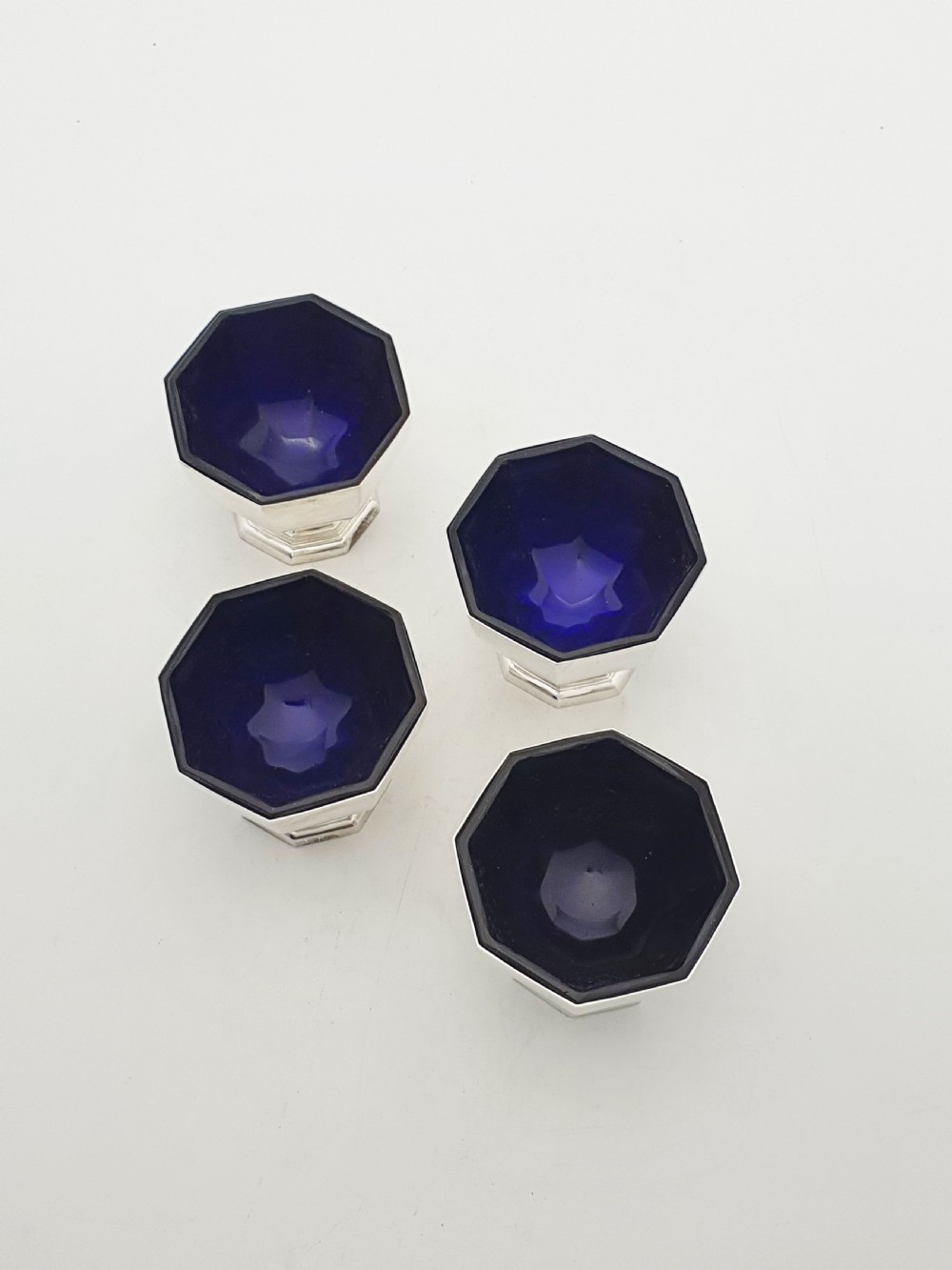 A set of four octagonal silver-plated salt cellars featuring dark cobalt blue glass liners on stepped pedestal bases. View II