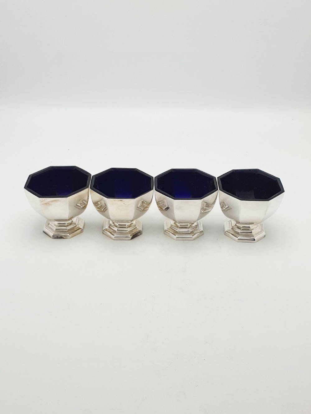 A set of four octagonal silver-plated salt cellars featuring dark cobalt blue glass liners on stepped pedestal bases. View III