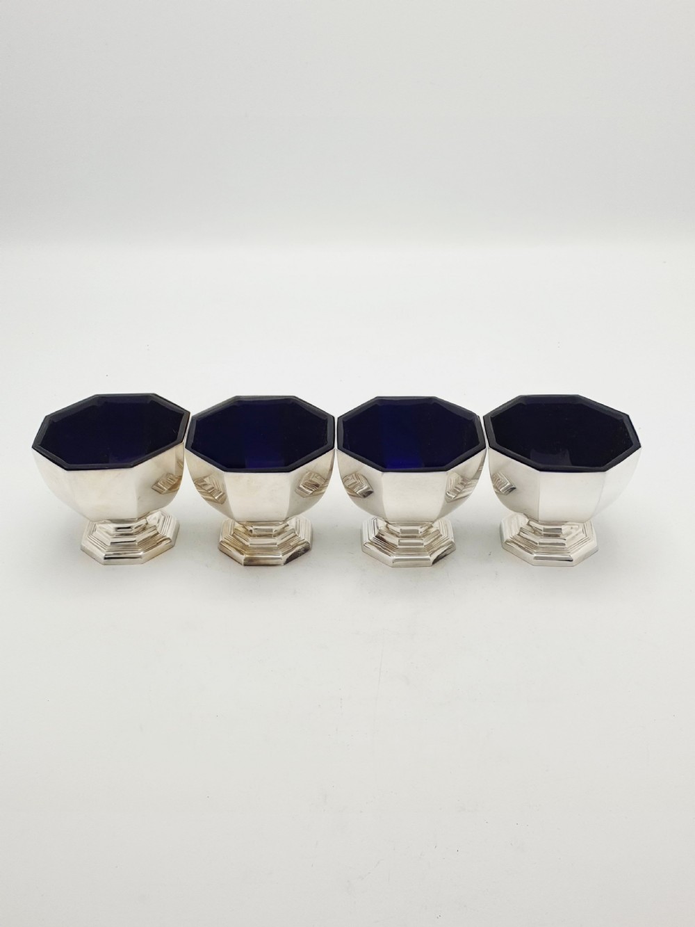A set of four octagonal silver-plated salt cellars featuring dark cobalt blue glass liners on stepped pedestal bases. View V