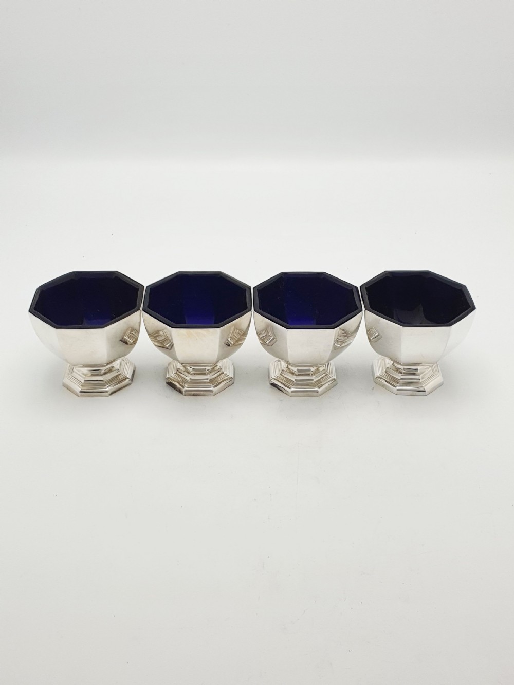 A set of four octagonal silver-plated salt cellars featuring dark cobalt blue glass liners on stepped pedestal bases. View VI