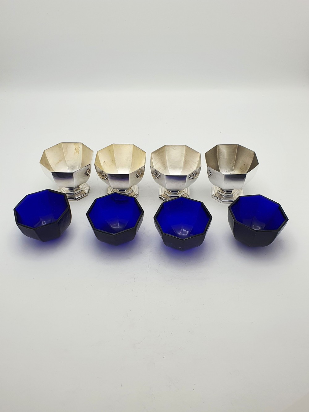 A set of four octagonal silver-plated salt cellars featuring dark cobalt blue glass liners on stepped pedestal bases. View VII
