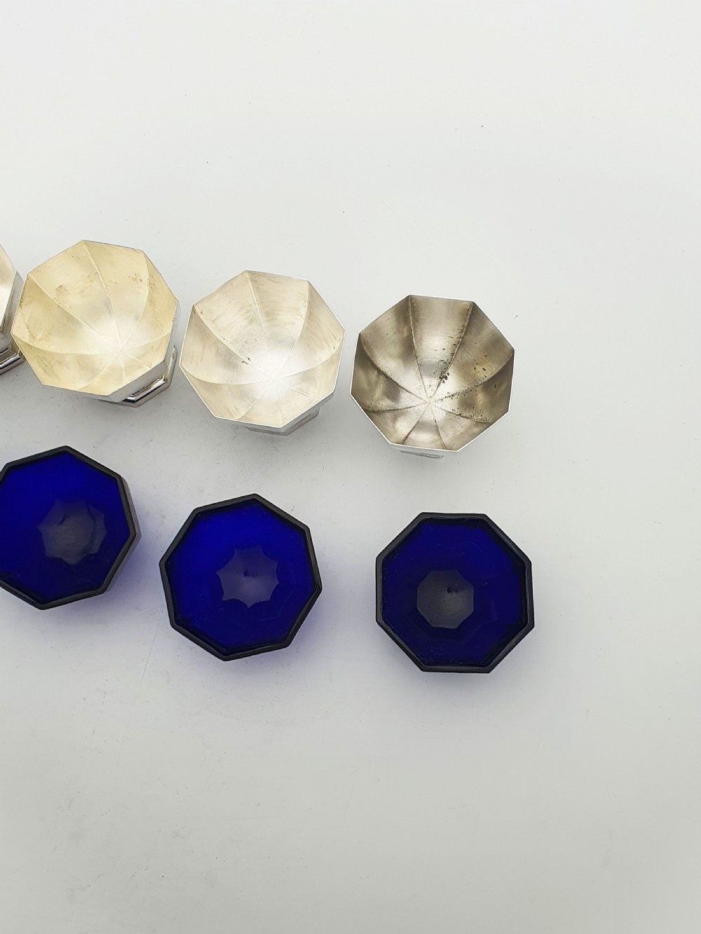 A set of four octagonal silver-plated salt cellars featuring dark cobalt blue glass liners on stepped pedestal bases. View IX