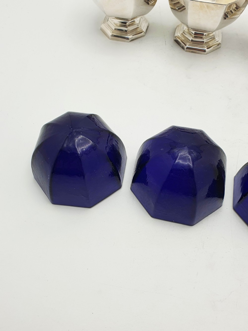 A set of four octagonal silver-plated salt cellars featuring dark cobalt blue glass liners on stepped pedestal bases. View X