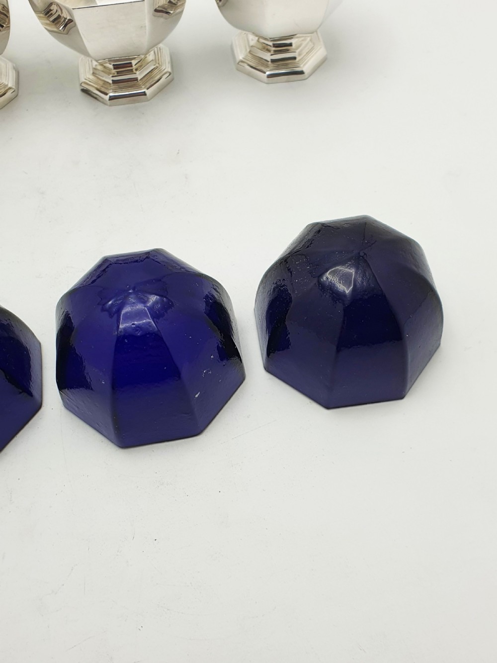 A set of four octagonal silver-plated salt cellars featuring dark cobalt blue glass liners on stepped pedestal bases. View XI