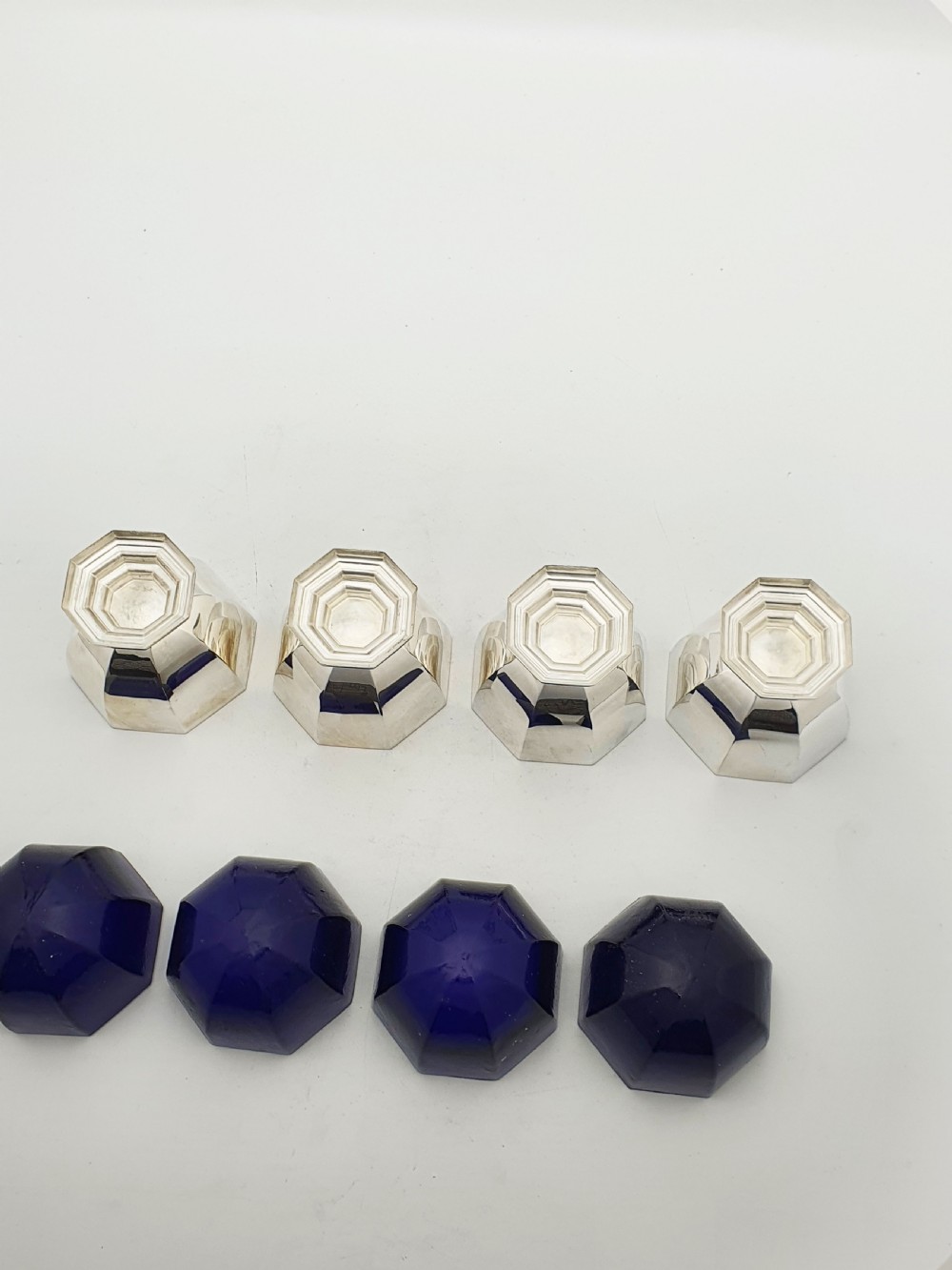 A set of four octagonal silver-plated salt cellars featuring dark cobalt blue glass liners on stepped pedestal bases. View XII
