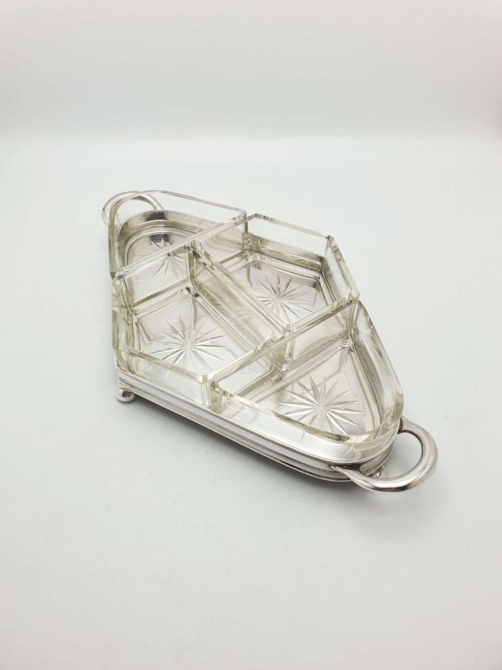 An Art Deco silver-plated tray featuring twin handles and ball feet, holding four fitted clear glass compartments with starburst cut patterns.