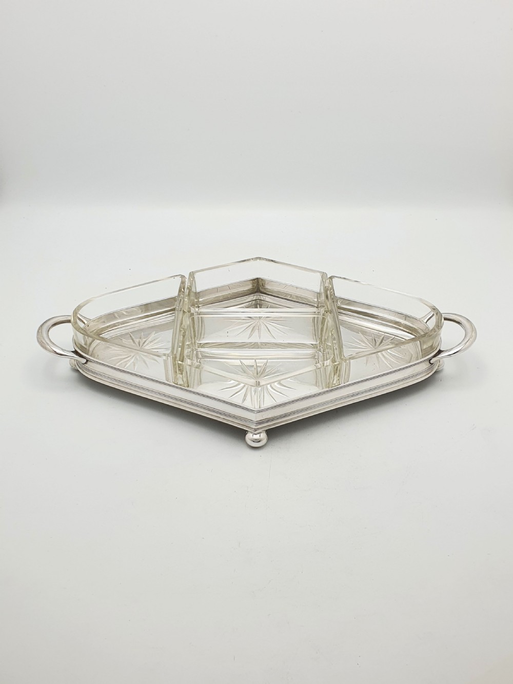 An Art Deco silver-plated tray featuring twin handles and ball feet, holding four fitted clear glass compartments with starburst cut patterns. View IV