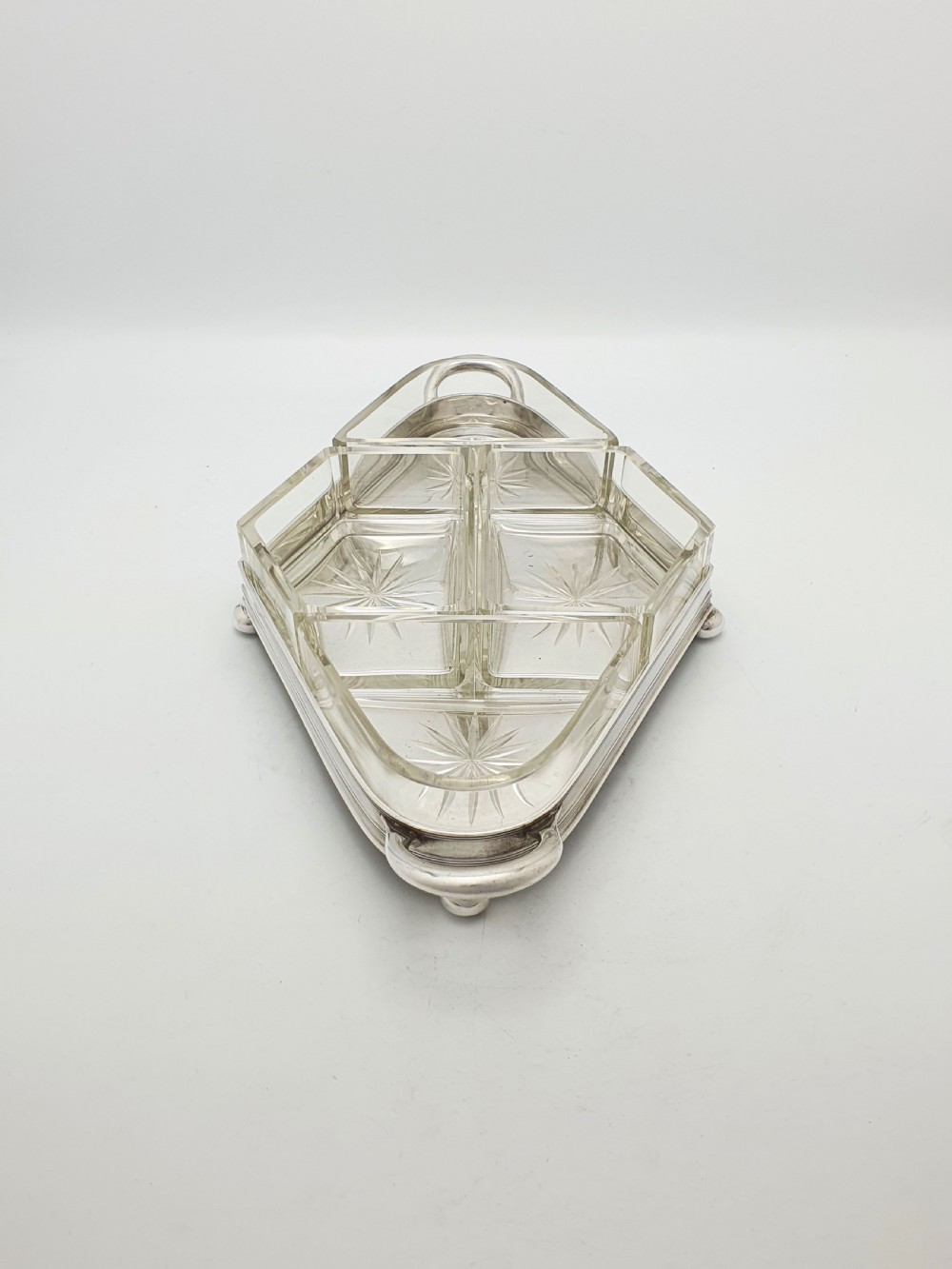 An Art Deco silver-plated tray featuring twin handles and ball feet, holding four fitted clear glass compartments with starburst cut patterns. View V