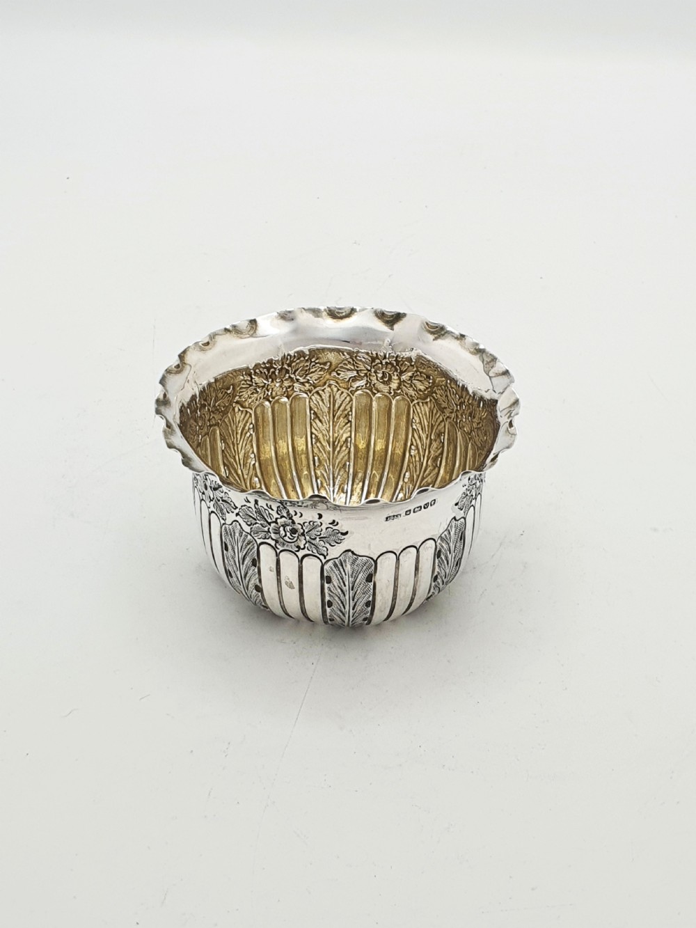 A small Late Victorian sterling silver bowl featuring fluted leaf decoration, floral engraving, a crimped rim, and a gilded interior.