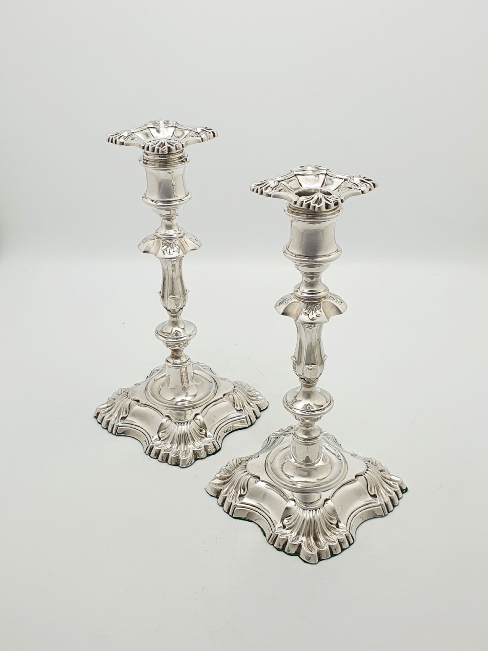 Pair of polished silver-plated Rococo Revival candlesticks with shell motifs and knopped stems on a plain background.