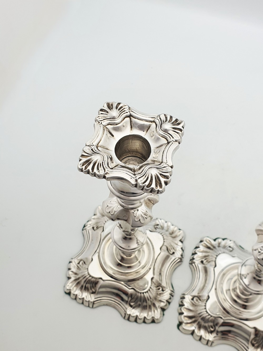 Pair of polished silver-plated Rococo Revival candlesticks with shell motifs and knopped stems on a plain background. View III