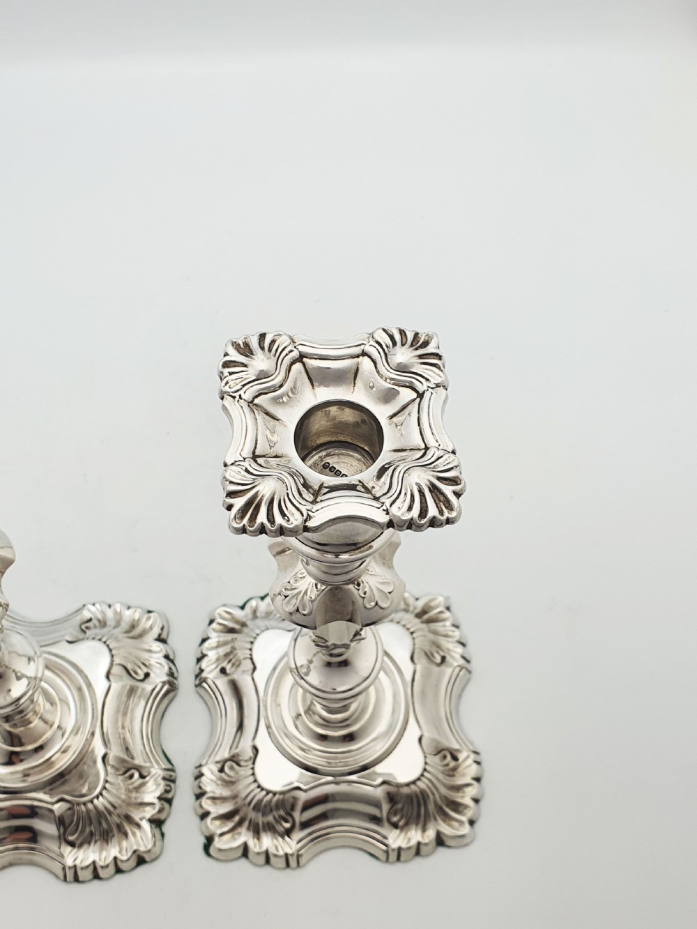 Pair of polished silver-plated Rococo Revival candlesticks with shell motifs and knopped stems on a plain background. View IV