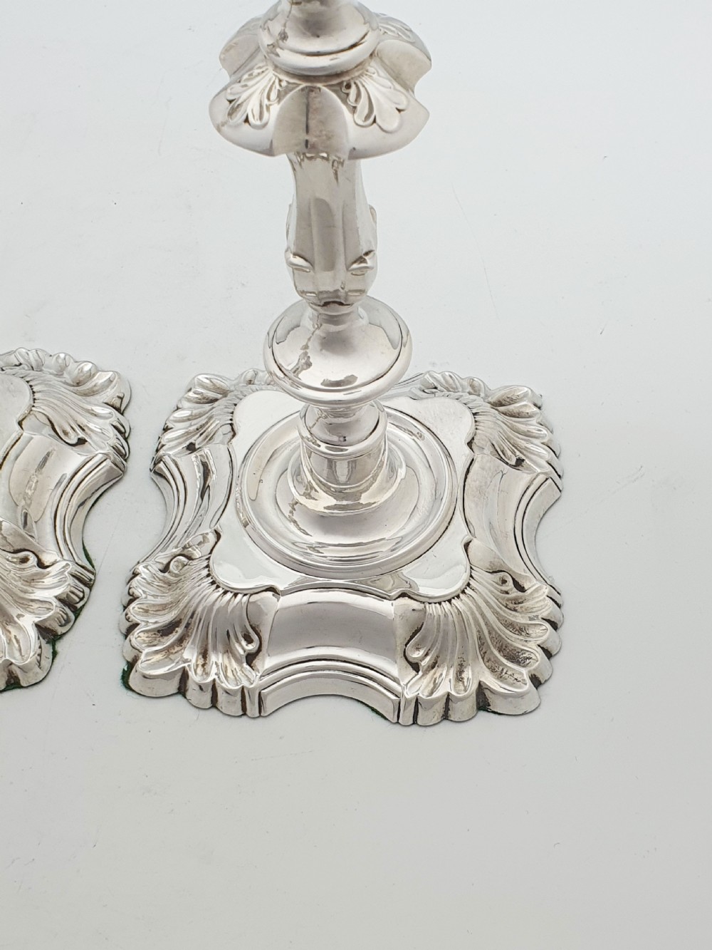 Pair of polished silver-plated Rococo Revival candlesticks with shell motifs and knopped stems on a plain background. View V
