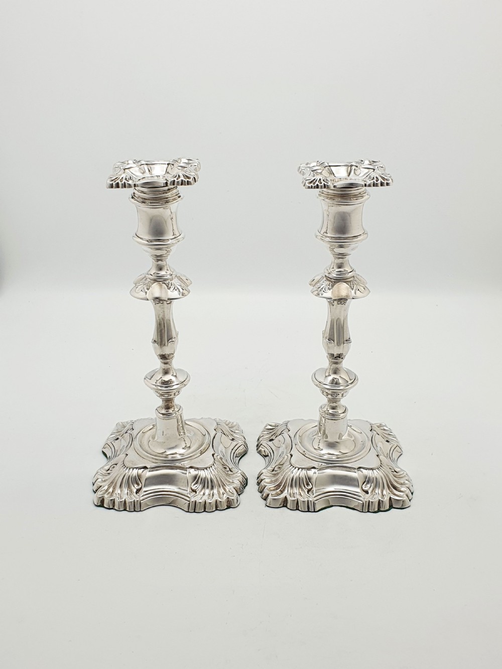 Pair of polished silver-plated Rococo Revival candlesticks with shell motifs and knopped stems on a plain background. View IX