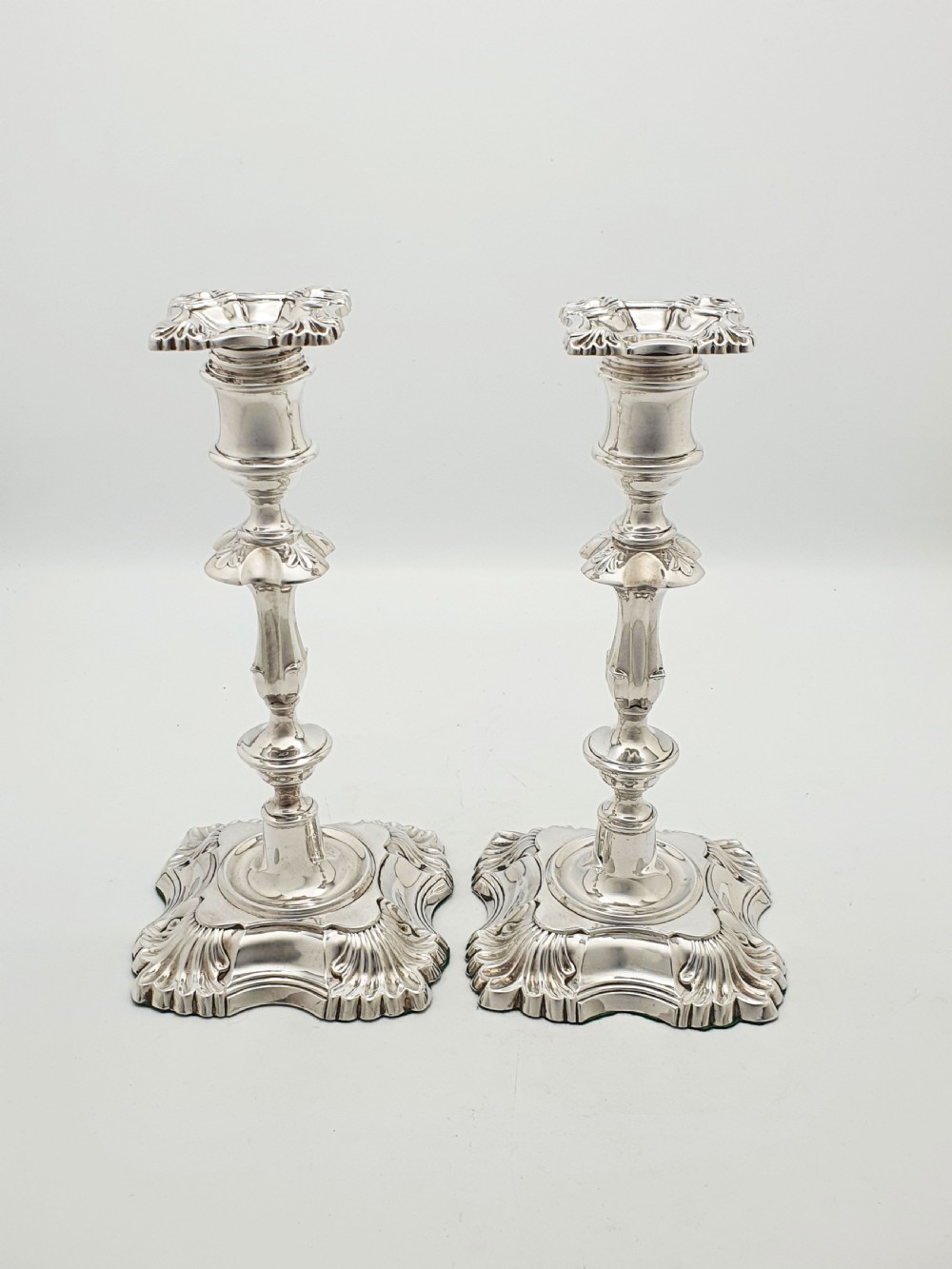 Pair of polished silver-plated Rococo Revival candlesticks with shell motifs and knopped stems on a plain background. View X